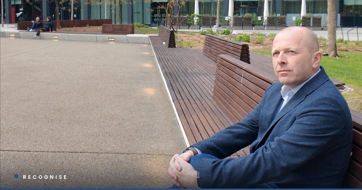 Chris Wilson seated alone on a bench in a corporate plaza, hands clasped, looking away